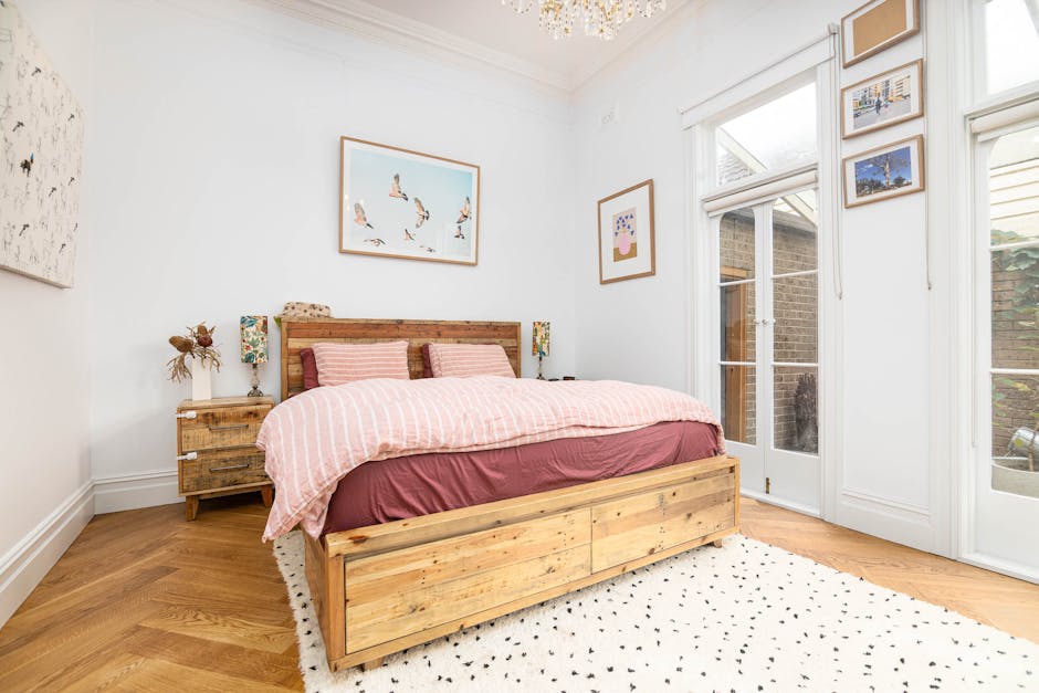 A bedroom featuring a wooden bed with a pink and white striped duvet cover and matching pillows. On either side of the bed are rustic wooden nightstands topped with decorative lamps. Hanging above the
